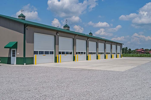 Row of insulated sectional overhead doors on a commercial metal building with yellow guard posts