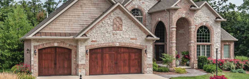 Stone and brick home with two stained wood-look carriage house garage doors